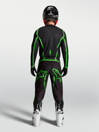 Jersey Fluid Apex V2 de Alpinestars, jersey de motocross, negro y verde fluorescente, vista trasera con botas blancas.