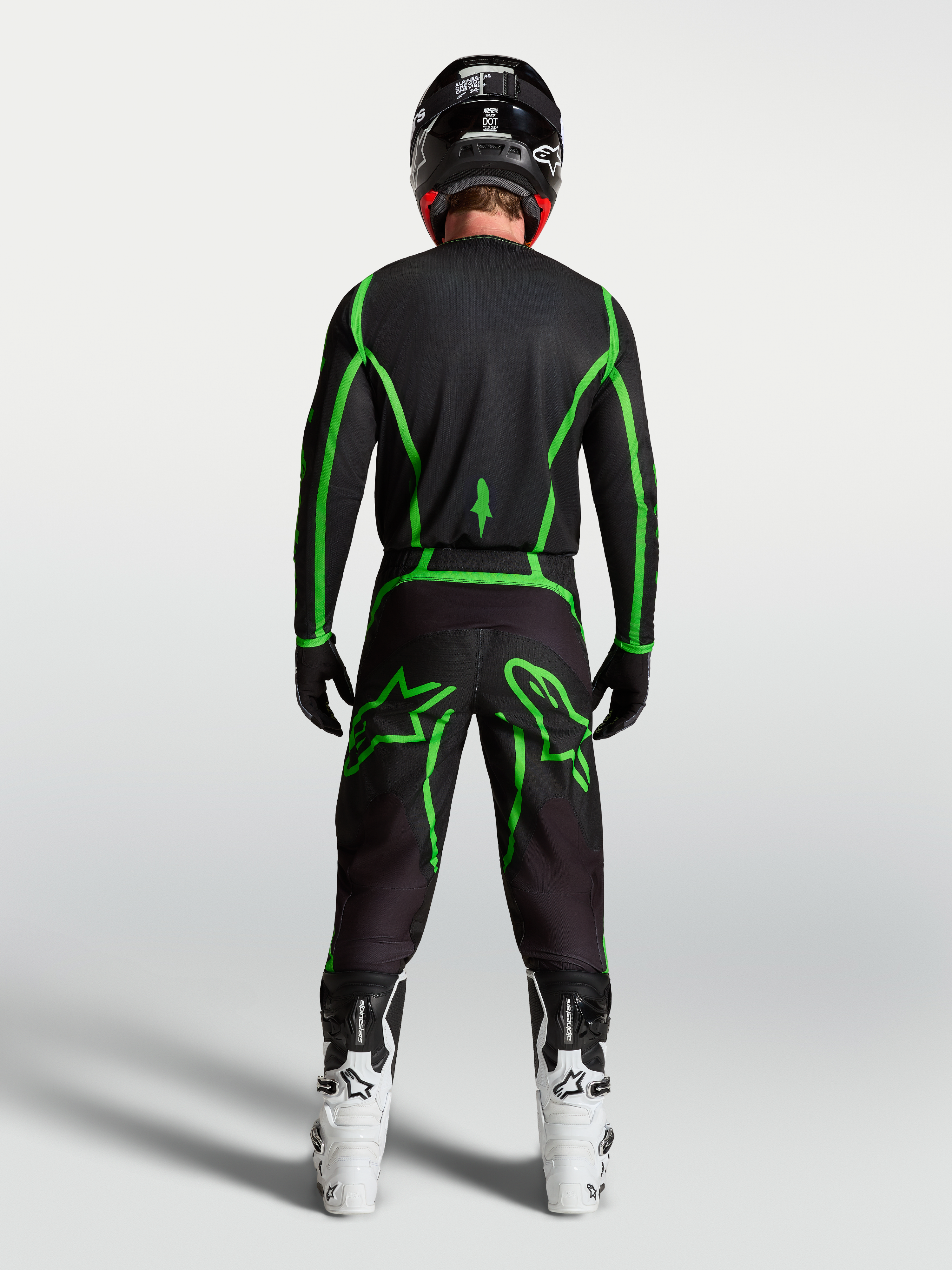 Jersey Fluid Apex V2 de Alpinestars, jersey de motocross, negro y verde fluorescente, vista trasera con botas blancas.