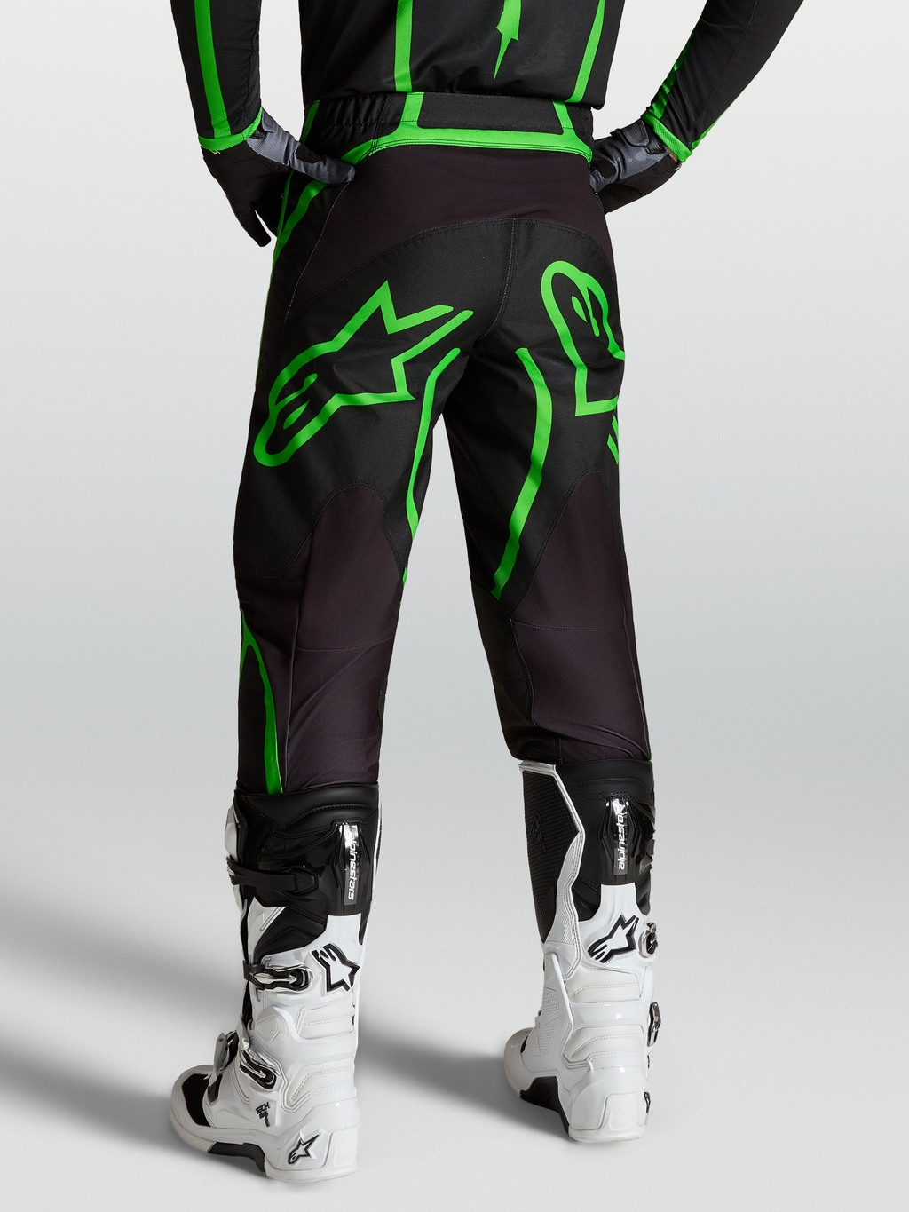 Alpinestars Fluid Apex V2, pantalones de motocross para hombre, negros y verde fluor, vista trasera sobre modelo con botas blancas