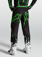 Alpinestars Fluid Apex V2, pantalones de motocross para hombre, negros y verde fluor, vista trasera sobre modelo con botas blancas