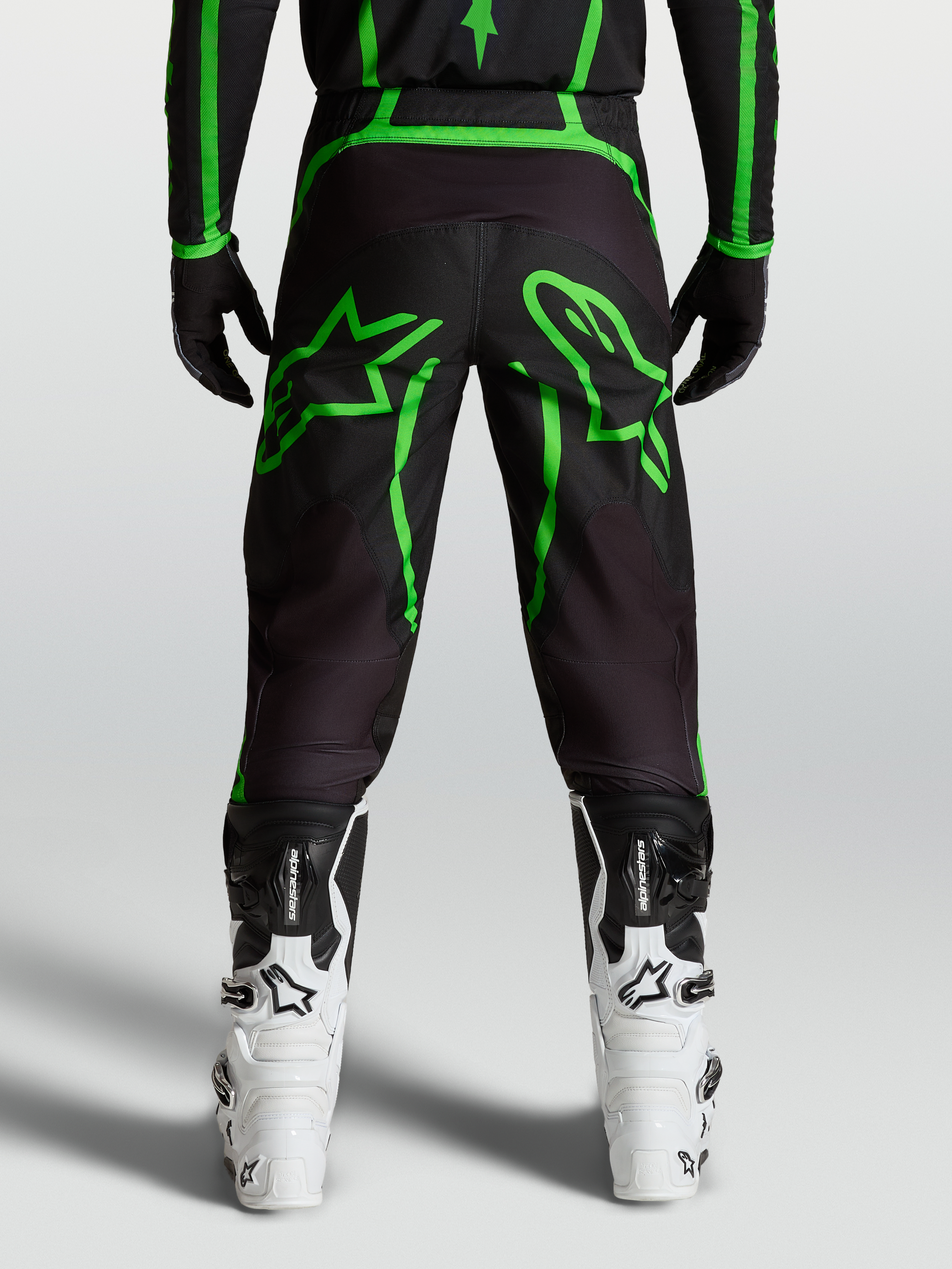 Alpinestars Pantalones Fluid Apex V2, pantalones de motocross para hombre, negros y verde flúor con gráficos de estrella, vista trasera en modelo.