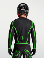 Alpinestars Jersey Fluid Apex V2, jersey de motocross, negro y verde fluorescente, vista trasera en modelo con cobertura trasera extendida para conducción off-road, diseño ligero y transpirable