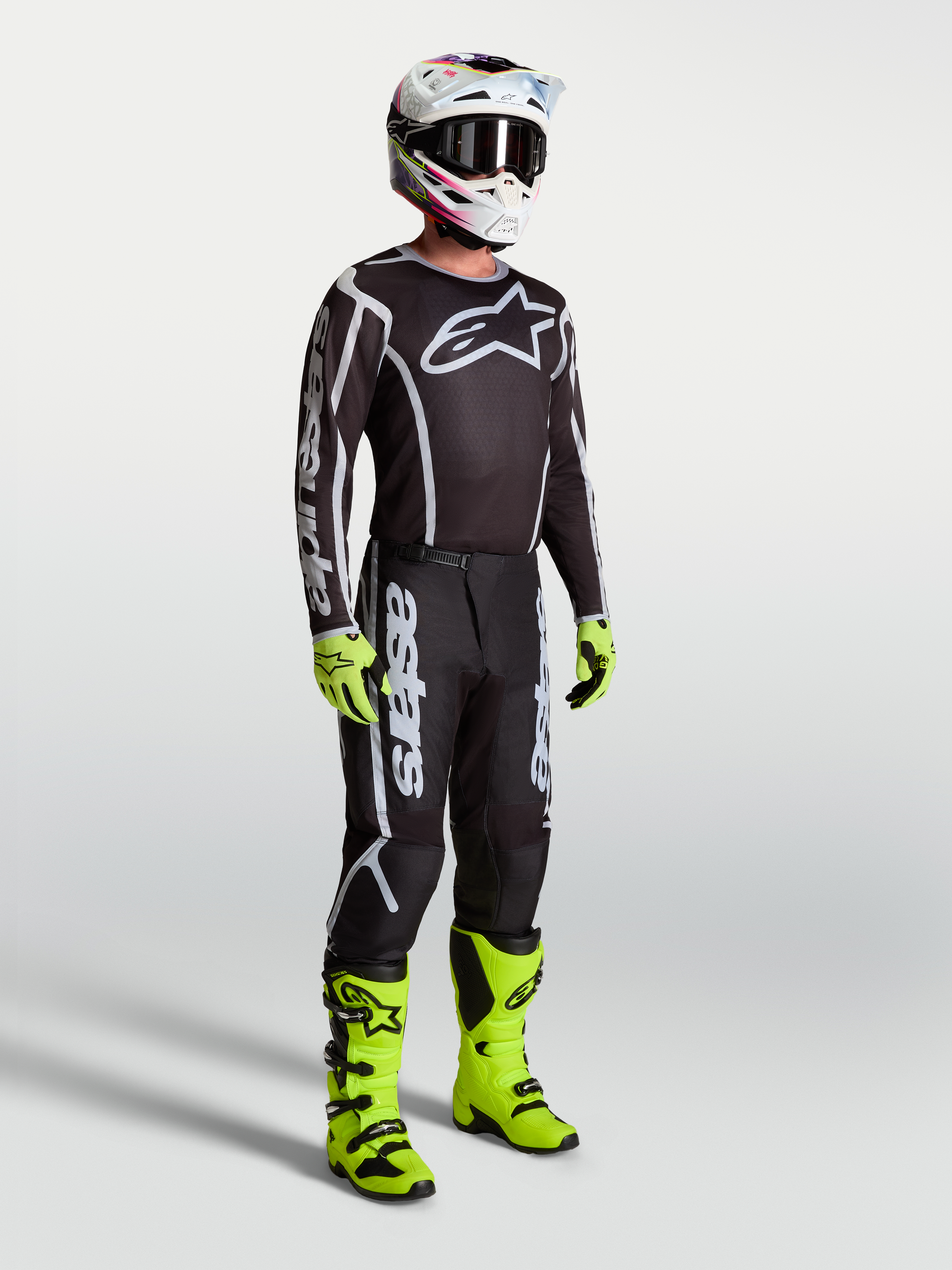Jersey Fluid Apex V2 de Alpinestars, ropa de motocross negra y plateada en modelo con botas y guantes verdes neón.