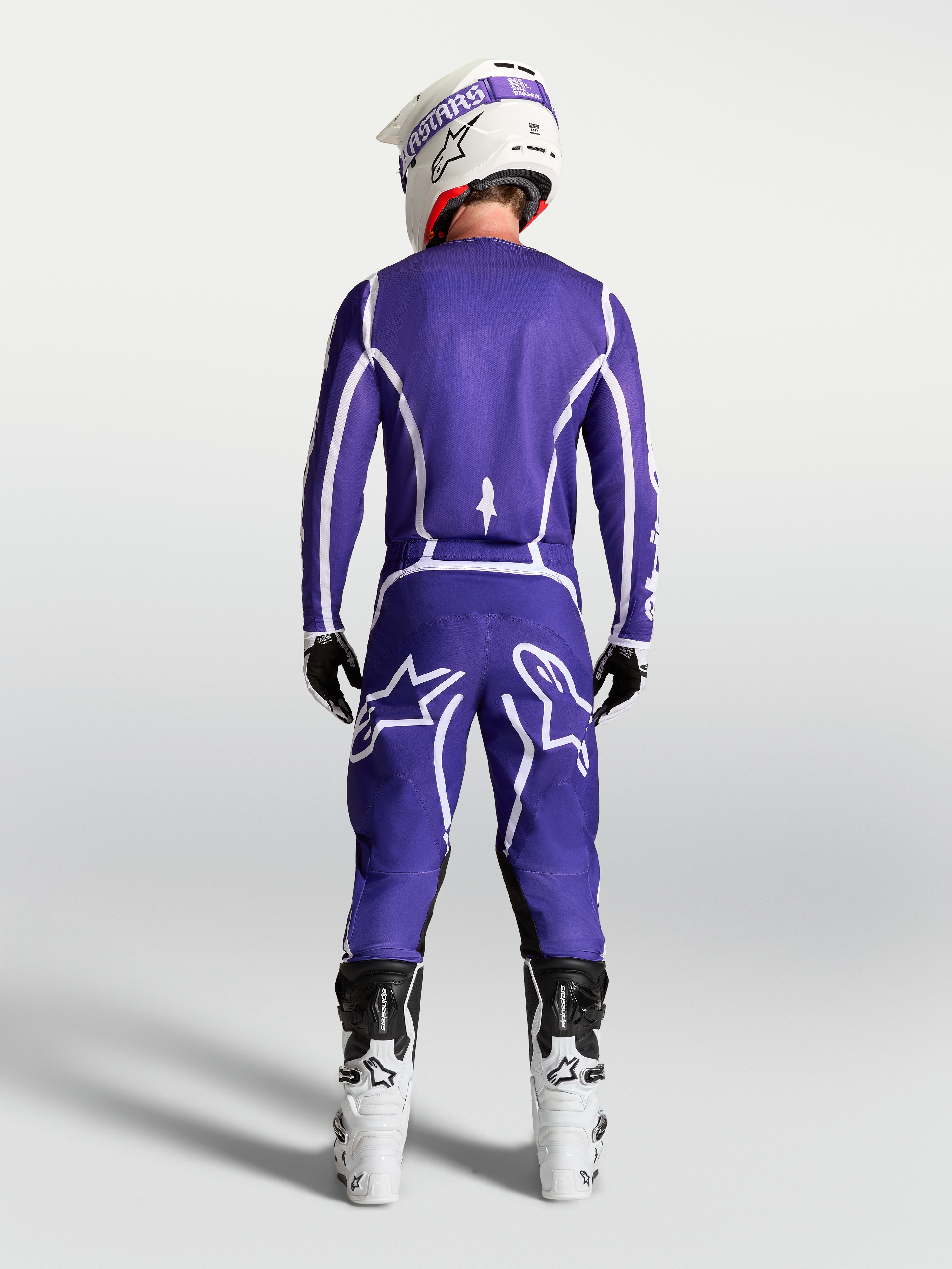 Jersey Alpinestars Fluid Apex V2 azul y blanco, vista trasera de piloto con pantalones de motocross y botas blancas.