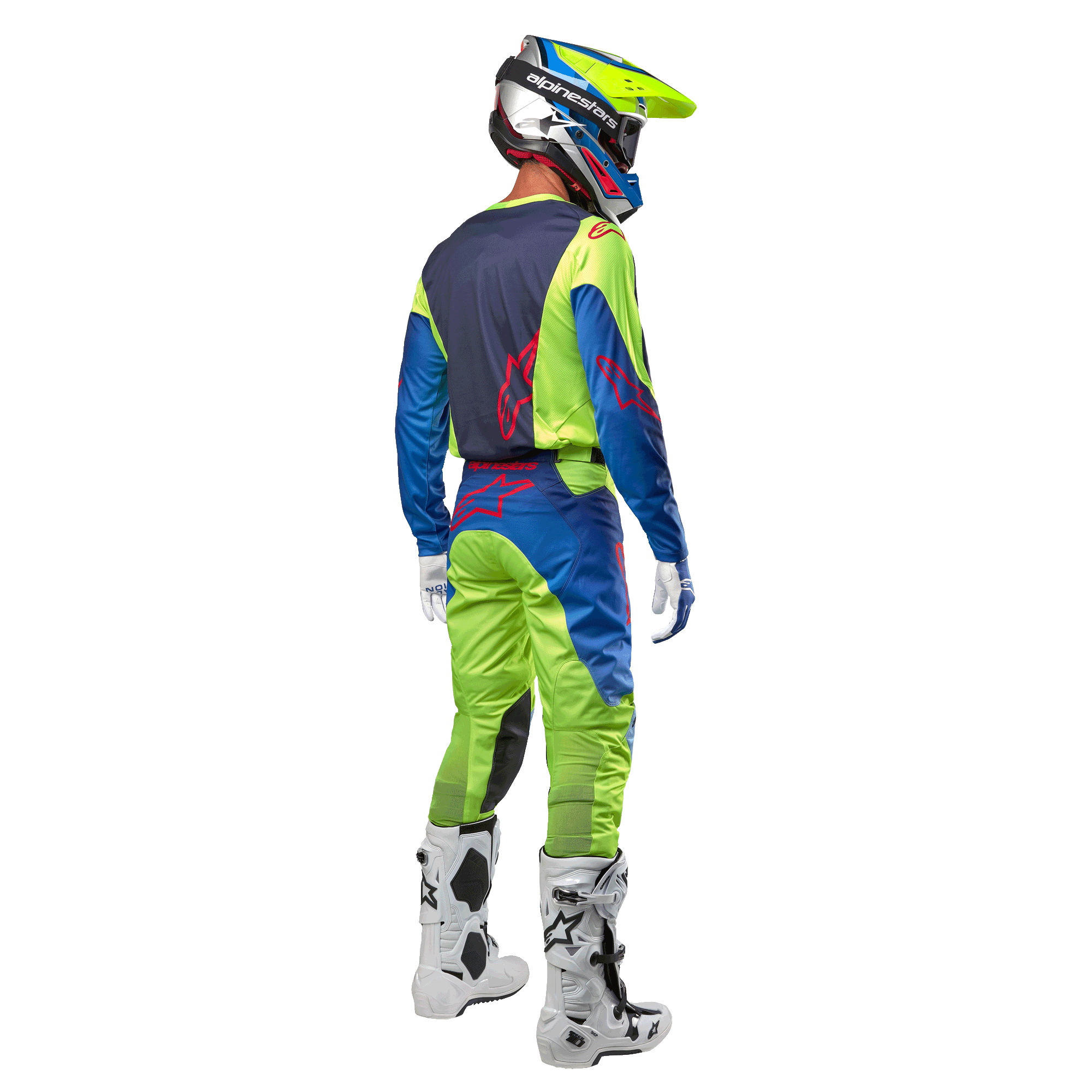 Piloto de motocross visto desde atrás con el jersey Alpinestars Racer Hoen 2024 en amarillo flúor y azul marino, pantalones de motocross a juego y botas blancas, mostrando el diseño posterior con logotipos rojos, equipamiento coordinado para conducción off-road profesional