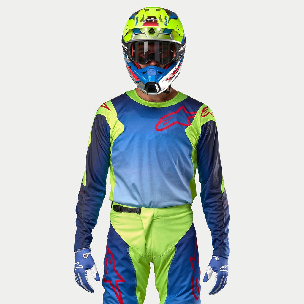 Alpinestars 2024 Racer Hoen Jersey, jersey de motocross, amarillo flúor y azul noche, vista frontal de un piloto con casco y equipamiento a juego, con un gran logotipo rojo en el pecho y paneles de malla transpirable