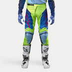 Pantalones Alpinestars Racer Hoen 2024, pantalones de motocross, color amarillo flúor y azul noche, combinados con botas de motocross blancas y negras y guantes azules, con logotipos rojos llamativos, paneles de rodilla en azul claro y un diseño ergonómico deportivo para conducción fuera de carretera