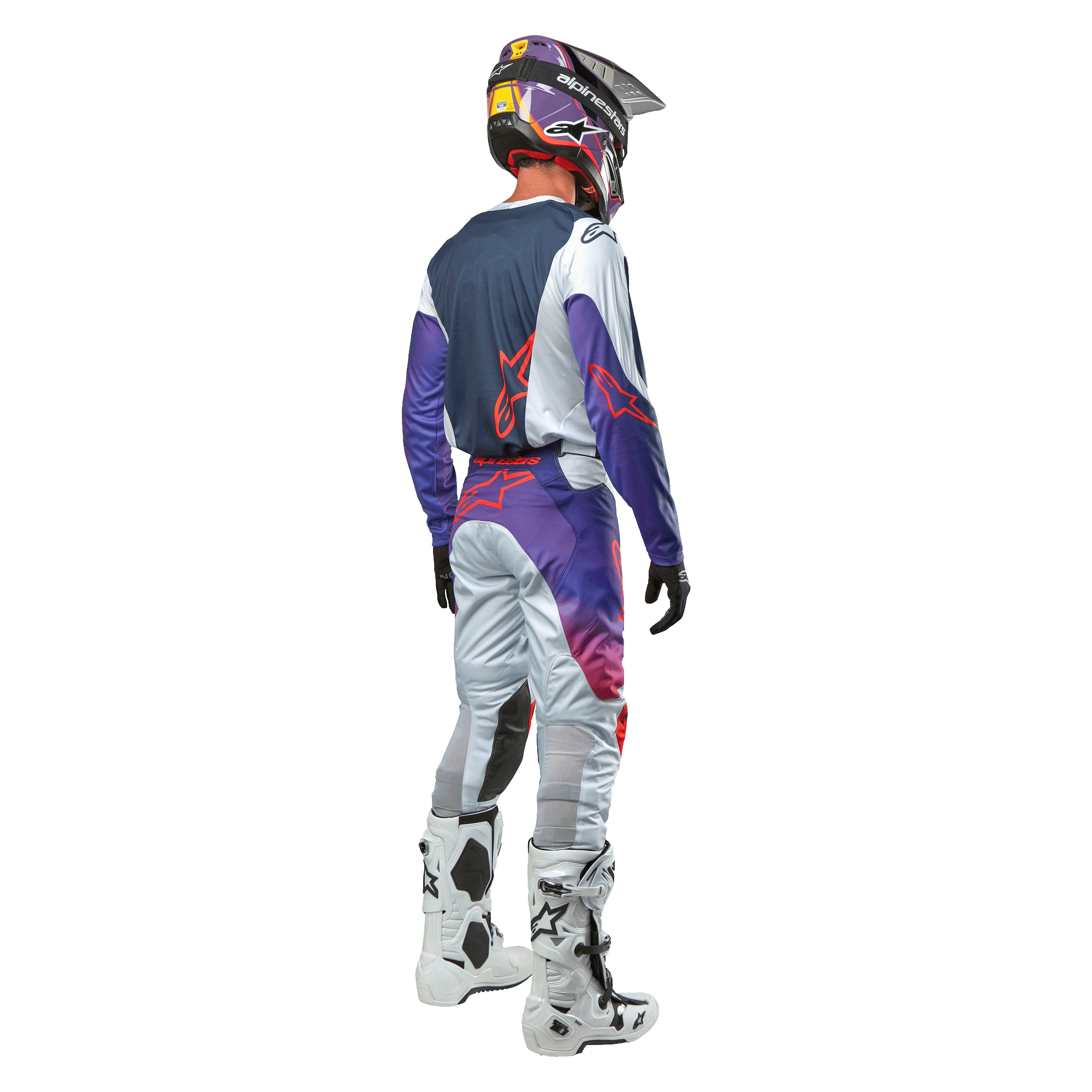 Piloto de motocross visto desde atrás con el jersey Alpinestars Racer Hoen 2024 en Gris Claro Naranja Intenso Negro, panel trasero azul marino con logo de estrella naranja, mangas moradas, combinado con pantalones de carreras a juego y botas blancas
