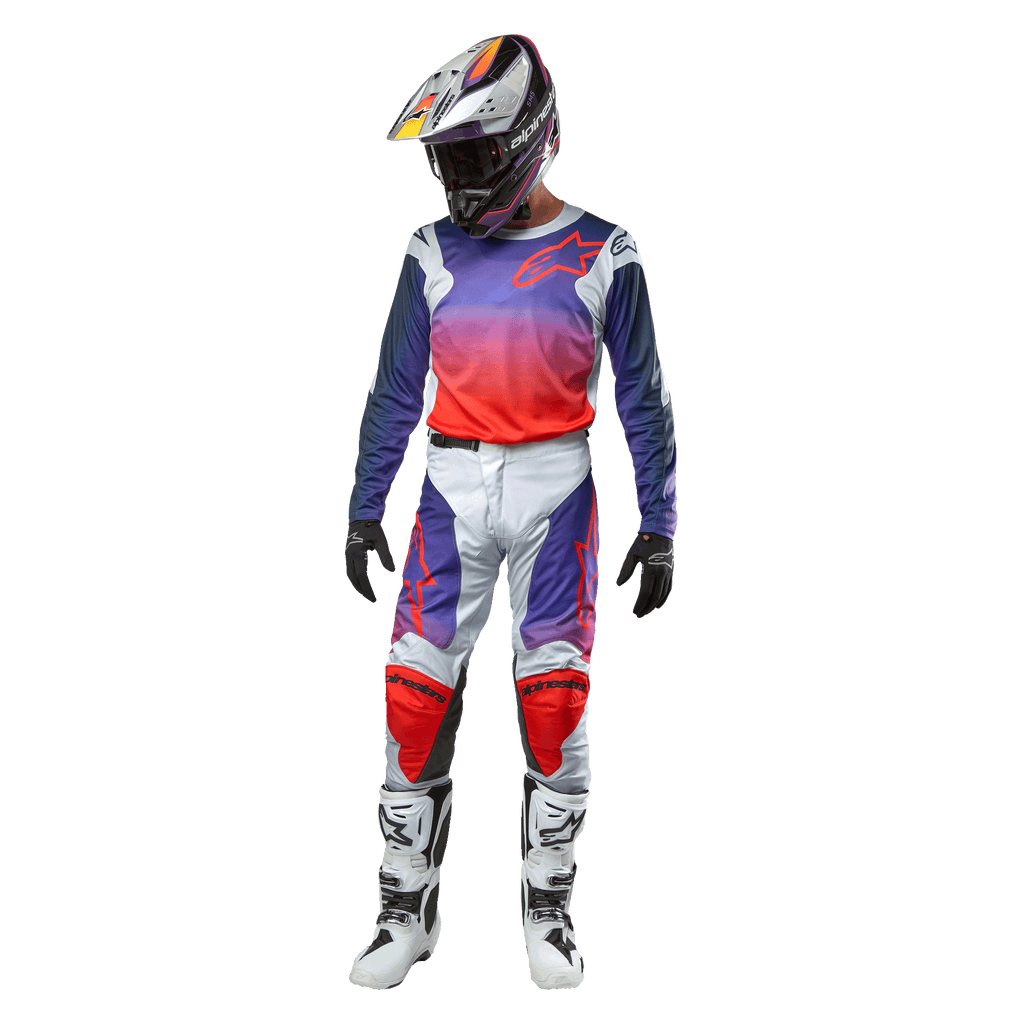 Piloto de motocross con equipamiento de competición completo, jersey Alpinestars 2024 Racer Hoen con degradado de púrpura a naranja intenso y hombros en gris claro, pantalones en gris claro a juego con acentos rojos y púrpuras, casco coordinado y botas blancas, atuendo completo para carreras off-road