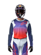 Alpinestars 2024 Racer Hoen Jersey en gris claro, naranja intenso y negro, jersey de motocross usado por un piloto con equipamiento a juego, con un vibrante degradado de colores y el logotipo de la estrella de Alpinestars en el pecho, diseñado para el rendimiento fuera de carretera.