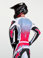 Alpinestars Fluid Drag, jersey de motocross para hombre, blanco y rojo con detalles negros y azules, politejido transpirable, vista trasera con casco y guantes