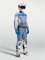 Jersey Racer Amber de Alpinestars, equipo de motocross para hombre en gris ceniza y azul UCLA, mostrado en modelo con casco y botas técnicas.