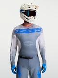 Alpinestars Jersey Racer Amber, equipo de motocross para hombre en gris y azul UCLA, con casco blanco y gafas de MX.
