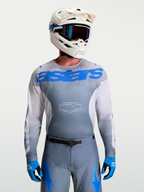 Alpinestars Jersey Racer Amber, equipo de motocross para hombre en gris y azul UCLA, con casco blanco y gafas de MX.