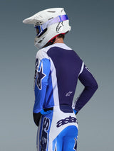 Motocross rider wearing the Alpinestars 2026 Racer Air Portl Jersey in Ucla Blue and White, rear view highlighting the breathable navy blue mesh back panel, worn with matching pants and a white Alpinestars helmet with blue goggles, coordinated motocross gear set.