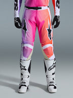 Alpinestars 2026 Racer Air Portl Pants, pantalones de motocross, degradado vibrante en púrpura, rosa y naranja, con logotipos de estrellas llamativos en los muslos, usados con botas de carreras blancas y guantes negros, diseñados para el pilotaje off-road de alto rendimiento