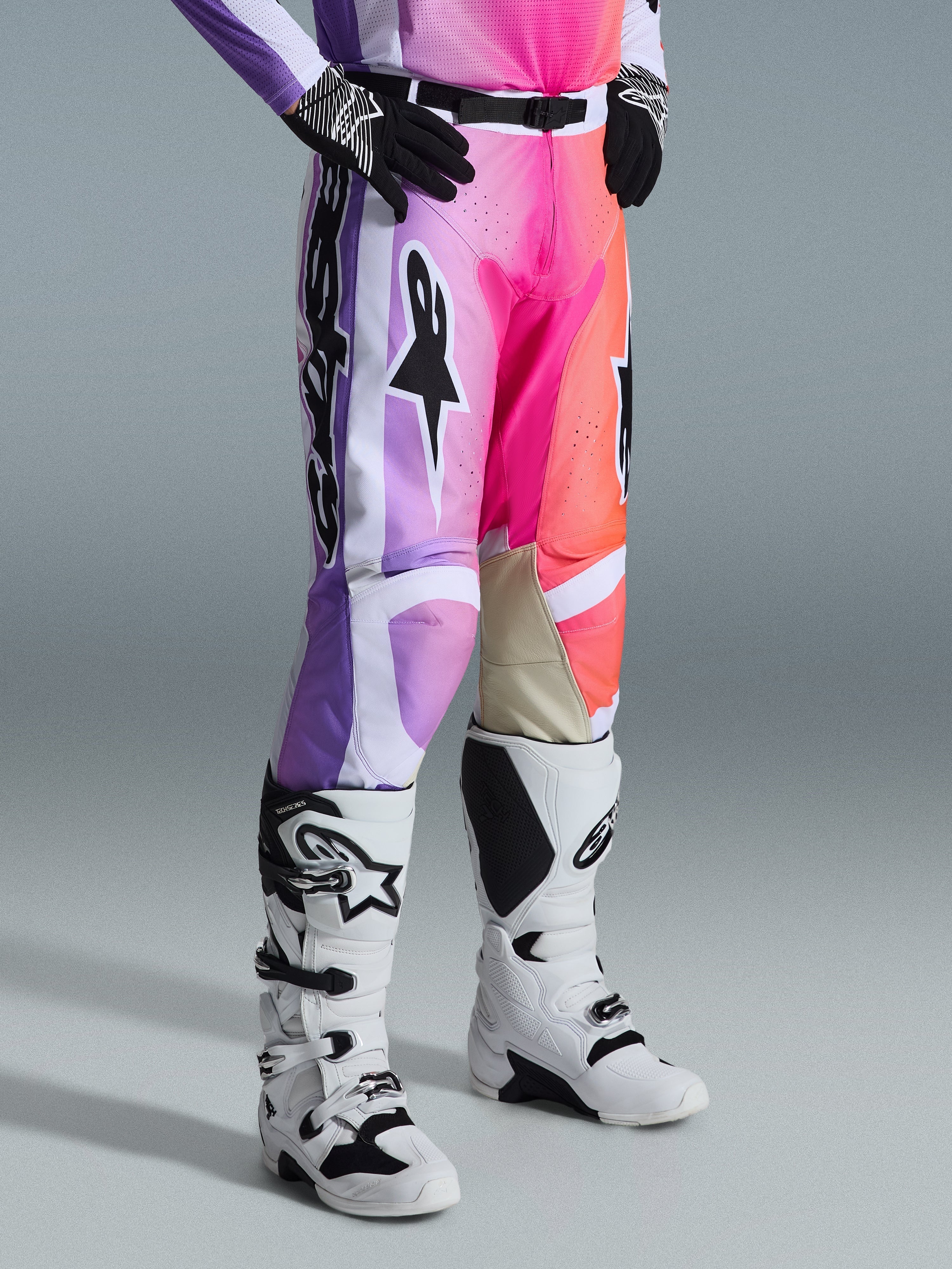 Alpinestars 2026 Racer Air Portl Pants, pantalones de motocross, gráfico multicolor con degradados en púrpura, rosa y naranja, combinados con botas de motocross blancas y negras y guantes negros, con diseño de ajuste de carrera y paneles de cuero tostado en el interior de las rodillas.