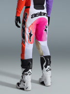 Alpinestars 2026 Racer Air Portl Pants, pantalones de motocross, multicolor con blanco, rosa brillante y naranja, vista trasera usados con botas Alpinestars blancas y negras, con logotipos llamativos y construcción de carrera duradera