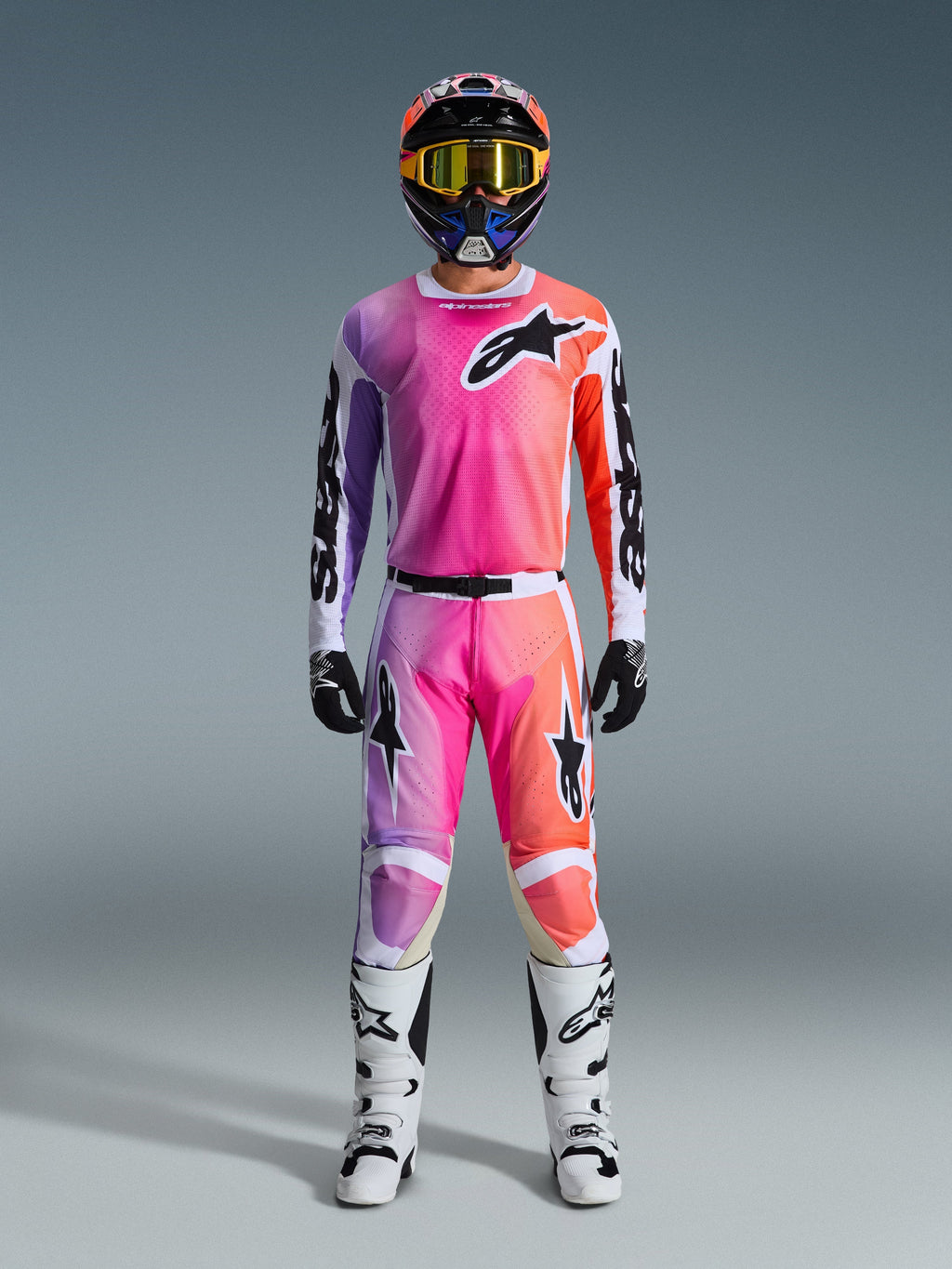 Piloto de motocross con equipamiento completo Alpinestars 2026 Racer Air Portl, con un diseño degradado en rosa, púrpura y naranja en los pantalones y el jersey, combinado con un casco a juego, gafas amarillas, botas blancas y guantes negros para un look off-road coordinado.