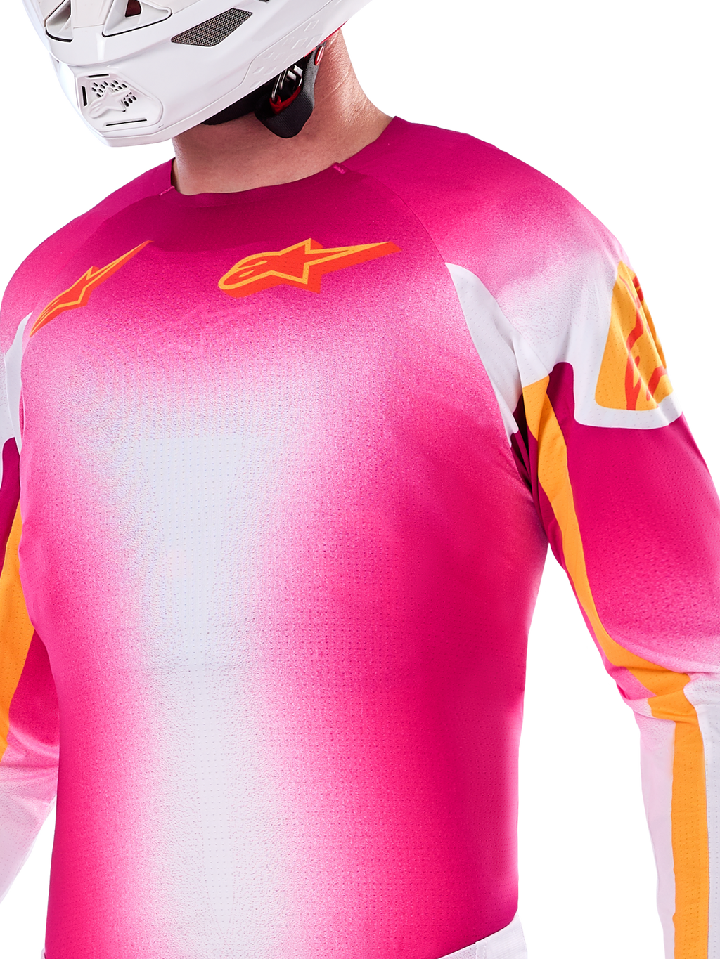 Alpinestars Supertech AFD MIG Edición Limitada, jersey de motocross en degradado rosa flúor y blanco, con logotipos Astars y detalles en las mangas en color naranja, usado por un piloto con casco blanco, ajuste atlético de competición