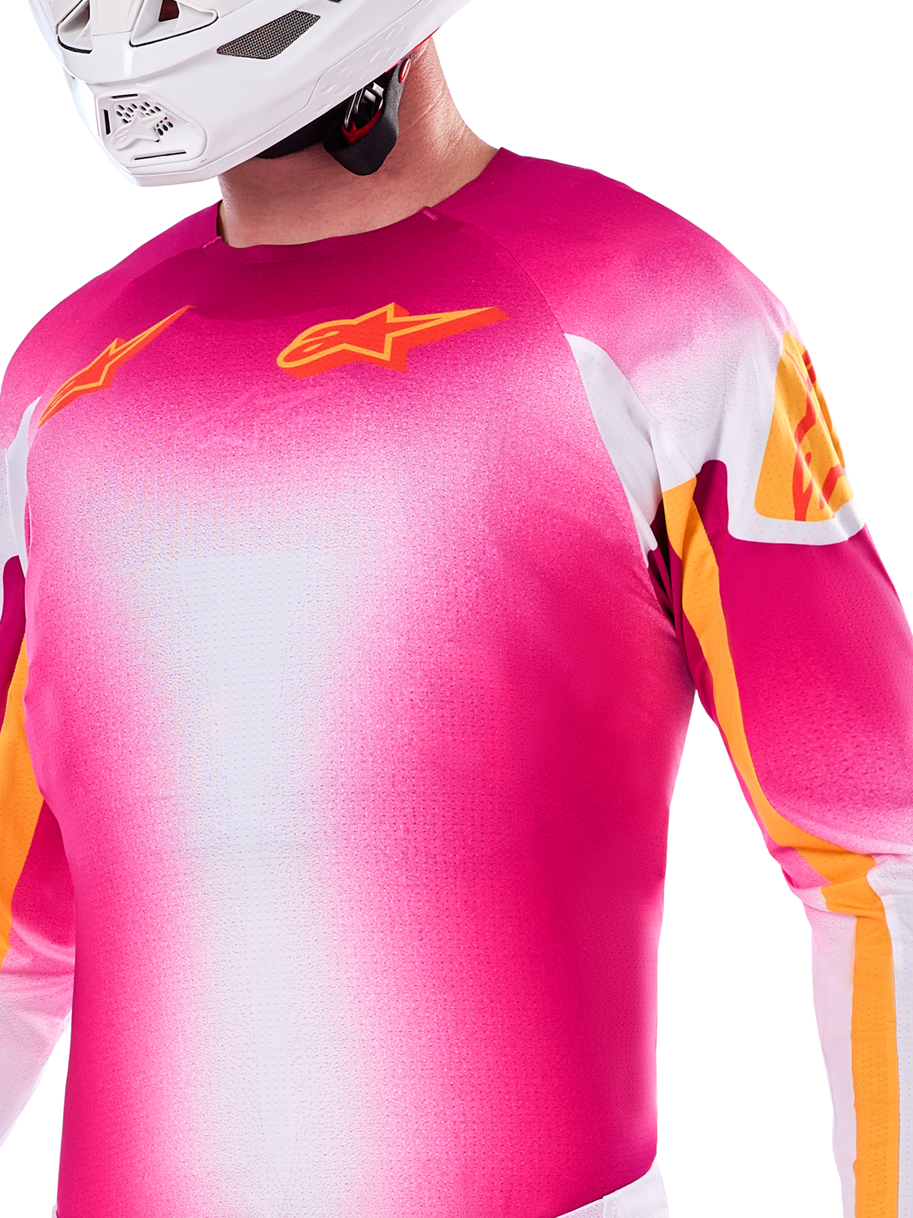 Alpinestars Supertech AFD MIG Edición Limitada, jersey de motocross en degradado rosa flúor y blanco, con logotipos Astars y detalles en las mangas en color naranja, usado por un piloto con casco blanco, ajuste atlético de competición