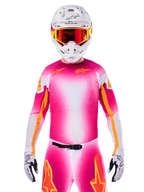 Jersey Alpinestars Limited Edition Supertech AFD MIG, camiseta de motocross rosa flúor y blanco con un degradado vibrante y logotipos de estrellas naranjas, usada como un kit de carreras completo con pantalones a juego, casco blanco y gafas rojas, ropa profesional para conducción en tierra