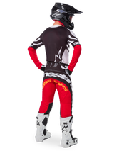 Motocross rider from the rear wearing the Alpinestars Limited Edition Techstar Deep Jersey in Black White High Red, featuring a black back with white star logo and red sleeves, paired with matching red and black pants, white and black boots, and a black helmet for a complete off-road racing outfit.