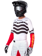 Alpinestars Techstar Deep Jersey Edición Limitada, jersey de motocross blanco con rayas negras onduladas y mangas inferiores rojas, combinado con casco negro, gafas de espejo, guantes blancos y negros y pantalones de carreras blancos, equipamiento de motocross de alto rendimiento