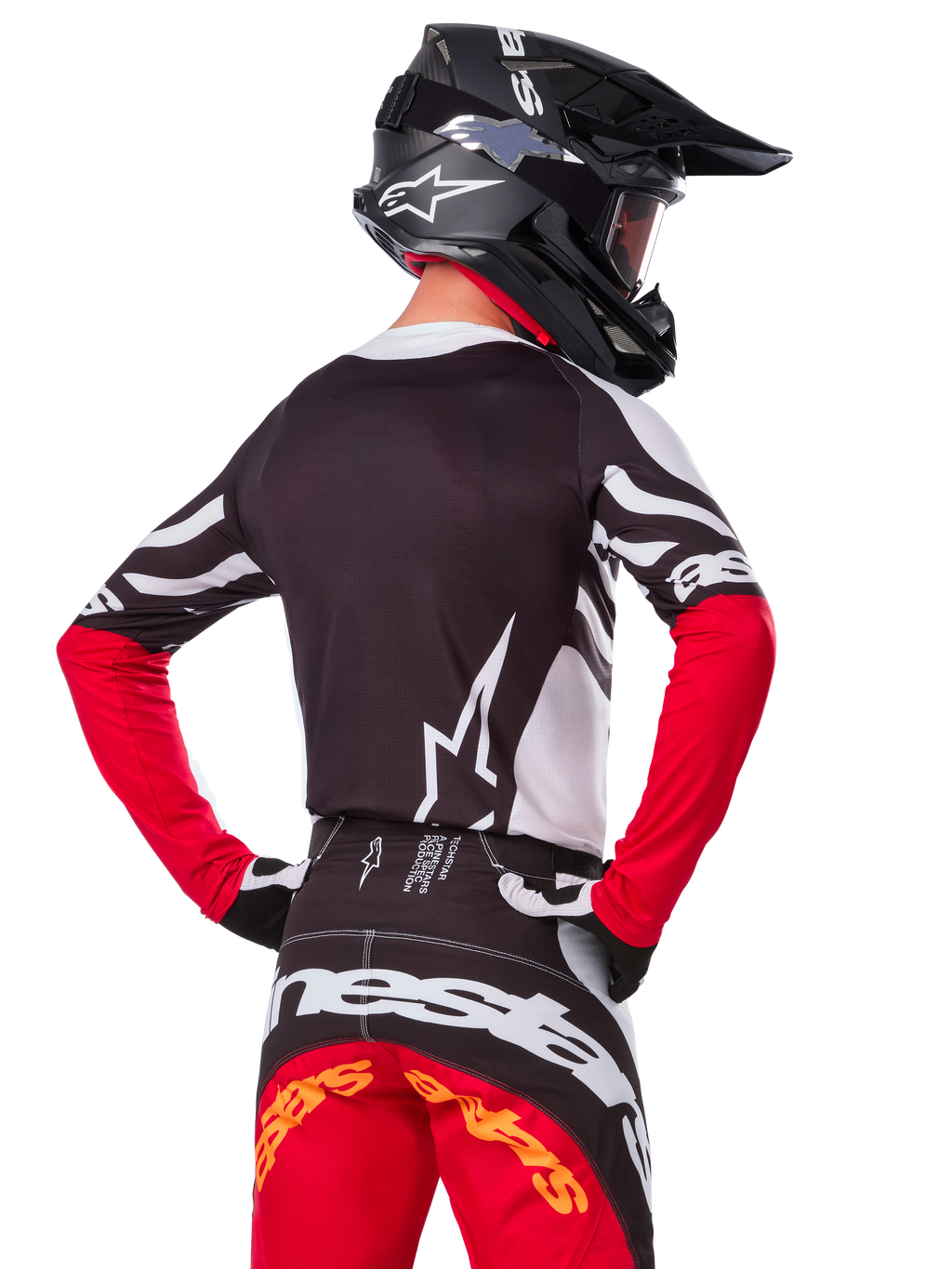 Piloto de motocross visto desde atrás vistiendo el jersey Alpinestars Techstar Deep Edición Limitada, negro, blanco y rojo intenso, con pantalones de carreras a juego y casco negro, ajuste atlético para un rendimiento todoterreno