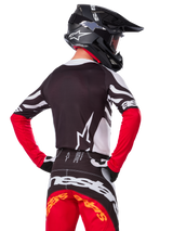 Motocross rider from the back wearing the Alpinestars Limited Edition Techstar Deep Jersey, Black White and High Red, with matching racing pants and a black helmet, athletic fit for off-road performance