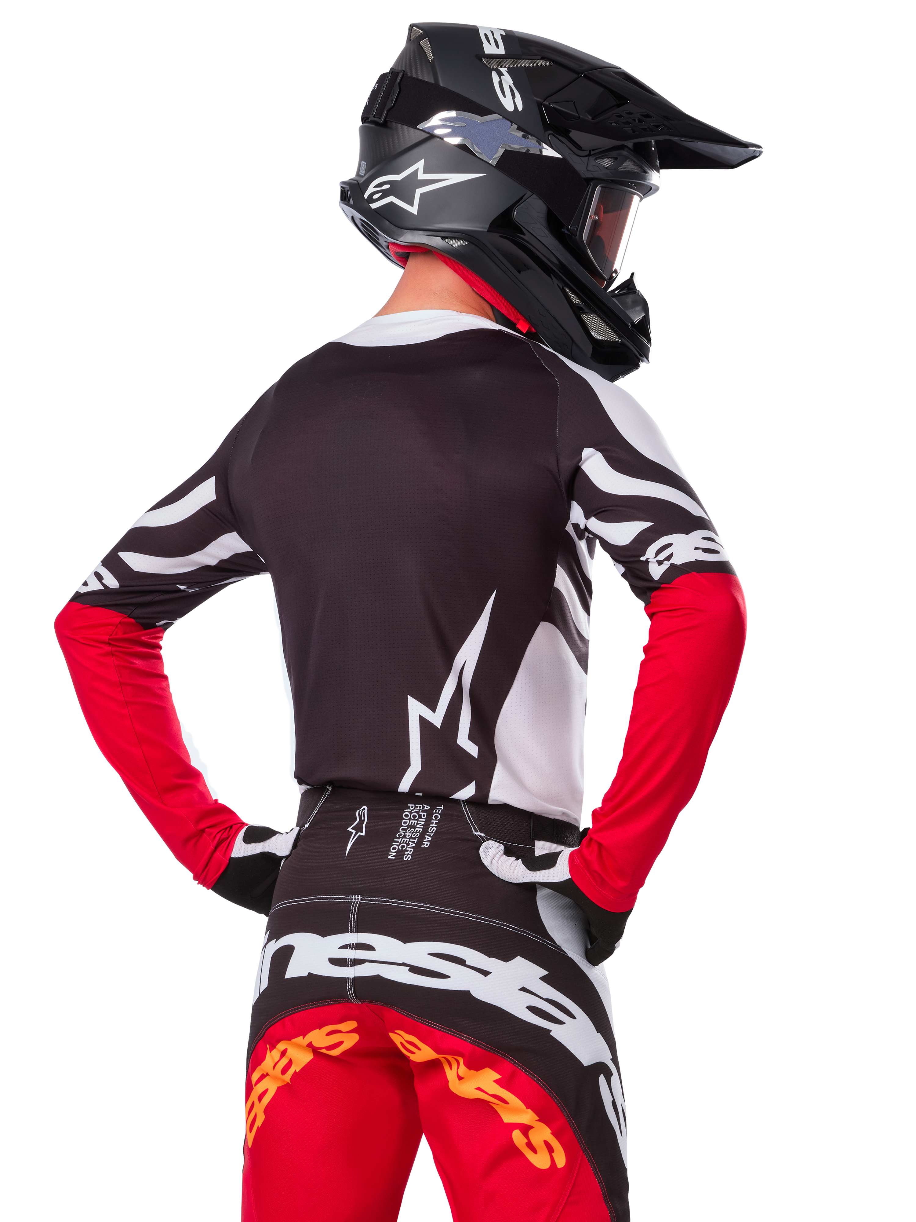 Piloto de motocross visto desde atrás vistiendo el jersey Alpinestars Techstar Deep Edición Limitada, negro, blanco y rojo intenso, con pantalones de carreras a juego y casco negro, ajuste atlético para un rendimiento todoterreno