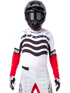Piloto de motocross con equipamiento completo de competición, Jersey Techstar Deep Edición Limitada en blanco y negro con mangas rojas, con gráficos ondulados y el logotipo de Alpinestars destacado, pantalones de motocross blancos, casco y gafas negros, conjunto coordinado para carreras todoterreno