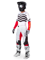 Piloto de motocross con equipamiento completo de carreras, Jersey Techstar Deep Edición Limitada con rayas onduladas blancas y negras y mangas rojas, pantalones blancos y rojos a juego, casco negro, botas blancas y negras, conjunto coordinado para carreras todoterreno