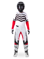 Piloto de motocross con el conjunto Alpinestars Techstar Deep Edición Limitada, jersey blanco con gráficos de ondas negras y mangas rojas, pantalones blancos y negros a juego con detalles rojos, casco negro con gafas oscuras y botas blancas, equipamiento profesional completo de competición todoterreno