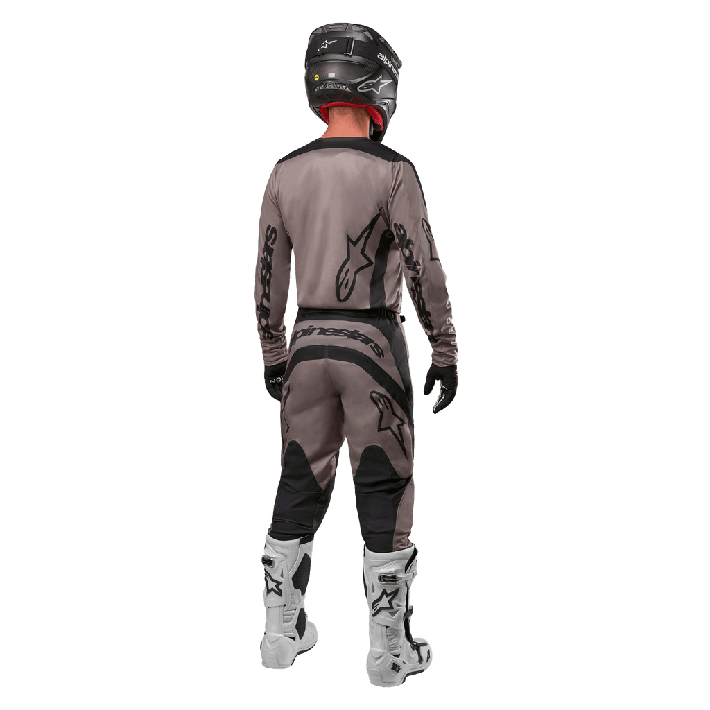 Alpinestars 2024 Fluid Lurv Jersey, jersey de motocross, Mud Black, vista trasera de un piloto de motocross con equipamiento de carreras a juego, casco negro y botas blancas, con logotipos negros de Alpinestars y un ajuste atlético para rendimiento todoterreno.