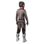 Alpinestars 2024 Fluid Lurv Jersey, jersey de motocross, Mud Black, vista trasera de un piloto de motocross con equipamiento de carreras a juego, casco negro y botas blancas, con logotipos negros de Alpinestars y un ajuste atlético para rendimiento todoterreno.