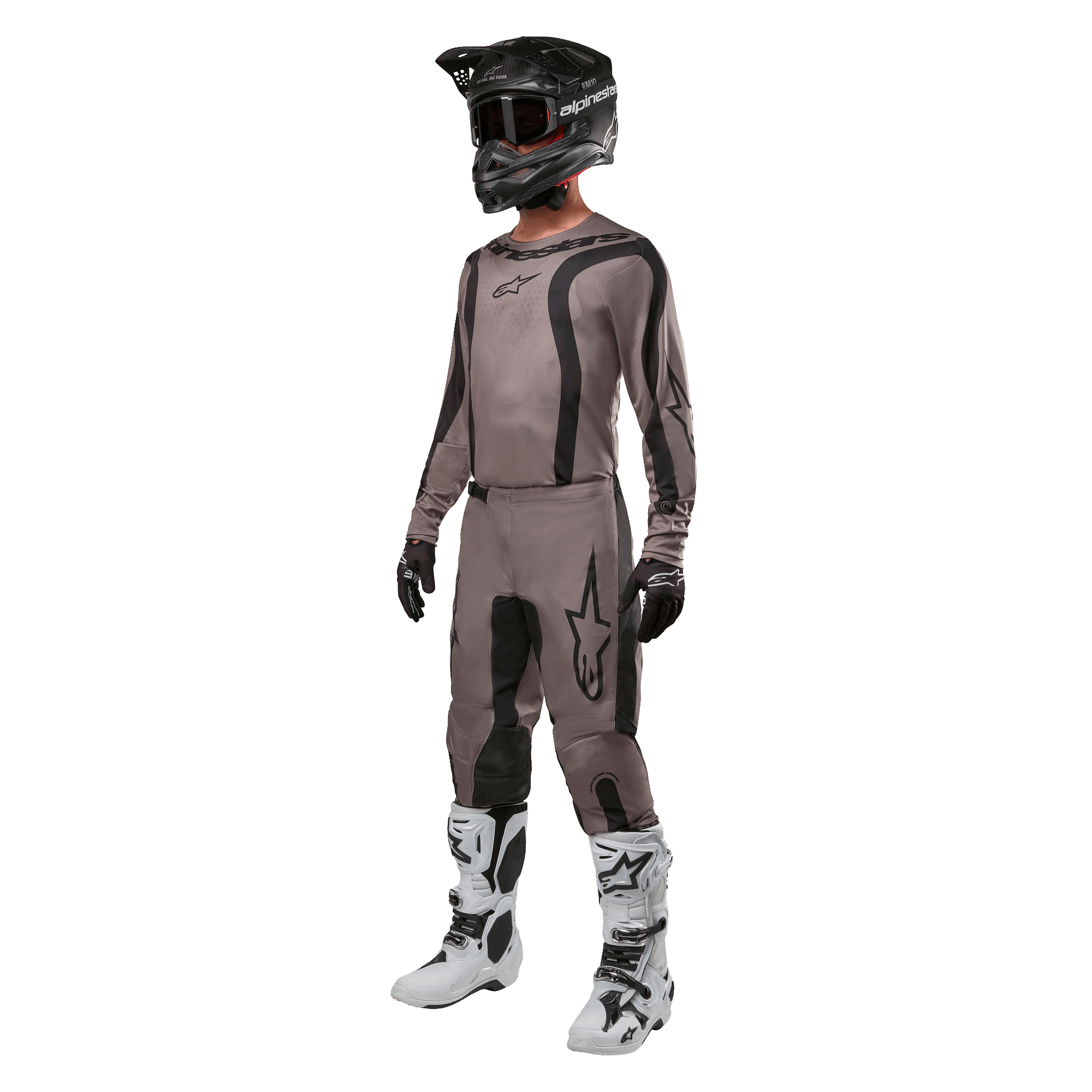 Piloto de motocross con equipamiento completo de carreras que incluye el jersey Alpinestars Fluid Lurv 2024 en color Mud Black, pantalones a juego, casco negro con gafas, botas blancas y negras, y guantes negros, conjunto coordinado para carreras todoterreno