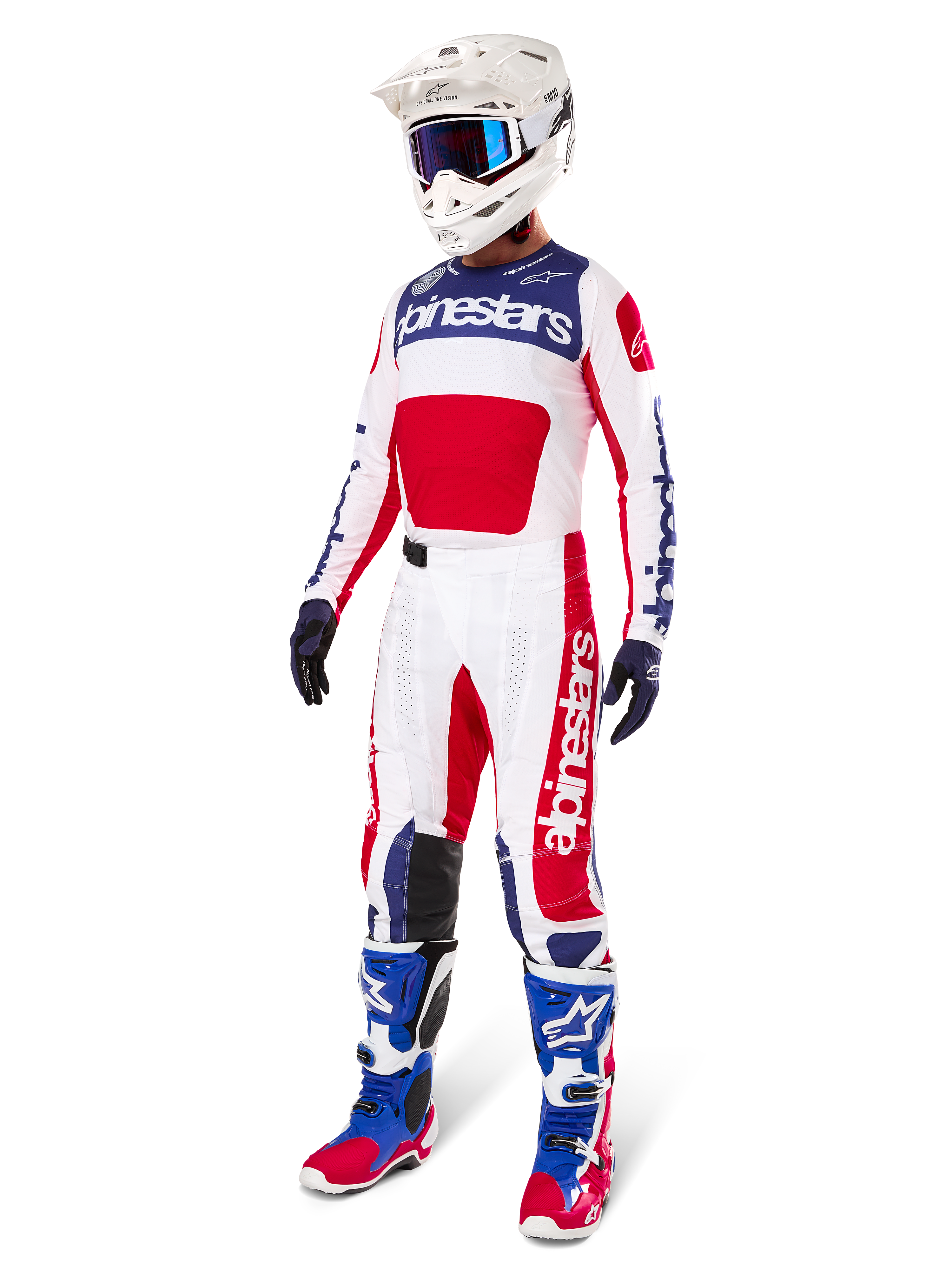 Piloto de motocross con equipamiento completo de carreras, que incluye el jersey Alpinestars Limited Edition Techstar Fortitude en rojo brillante, blanco y azul. Pantalones de motocross a juego, casco blanco con gafas azules y botas azules y rojas, proporcionando un aspecto coordinado para competiciones todoterreno.