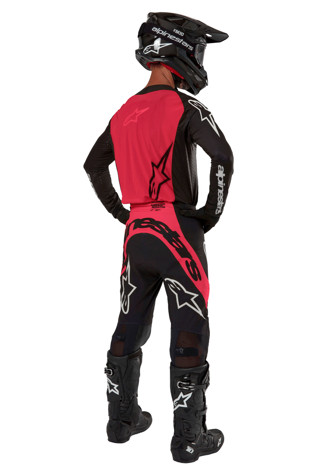 Piloto de motocross desde atrás con el Jersey Supertech Ward 2024 en Negro Red Berry, con un vibrante panel trasero rojo y mangas negras con la marca Alpinestars en blanco. Combinado con pantalones de motocross a juego, botas Tech 10 negras y un casco de fibra de carbono negro para un conjunto de equipamiento de carreras profesional coordinado.