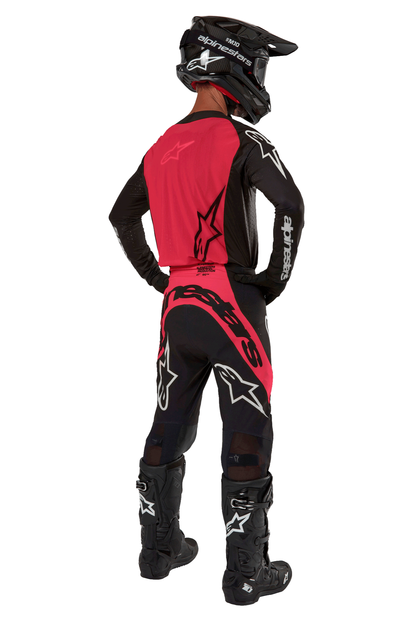 Piloto de motocross desde atrás con el Jersey Supertech Ward 2024 en Negro Red Berry, con un vibrante panel trasero rojo y mangas negras con la marca Alpinestars en blanco. Combinado con pantalones de motocross a juego, botas Tech 10 negras y un casco de fibra de carbono negro para un conjunto de equipamiento de carreras profesional coordinado.