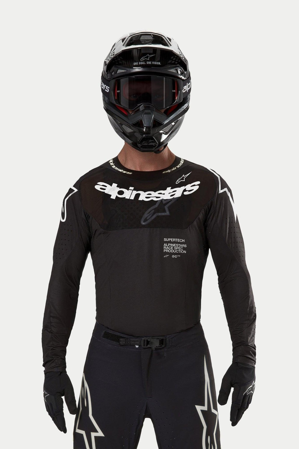 Alpinestars Supertech Ward Jersey 2024, jersey de motocross negro, ajuste de carrera atlético con logotipo blanco en el pecho, perforaciones cortadas con láser y texto 'Supertech Race Spec', usado por un piloto con casco y gafas negras para carreras todoterreno