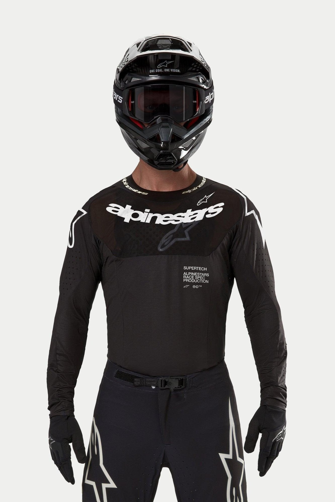 Alpinestars Supertech Ward Jersey 2024, jersey de motocross negro, ajuste de carrera atlético con logotipo blanco en el pecho, perforaciones cortadas con láser y texto 'Supertech Race Spec', usado por un piloto con casco y gafas negras para carreras todoterreno