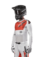 Alpinestars Supertech Ward Jersey 2024, jersey de motocross, blanco y naranja intenso, con panel rojo en el pecho y logo de estrella blanco, mangas largas con perforaciones cortadas con láser, usado con casco negro y guantes blancos, equipamiento de motocross con ajuste atlético de carrera