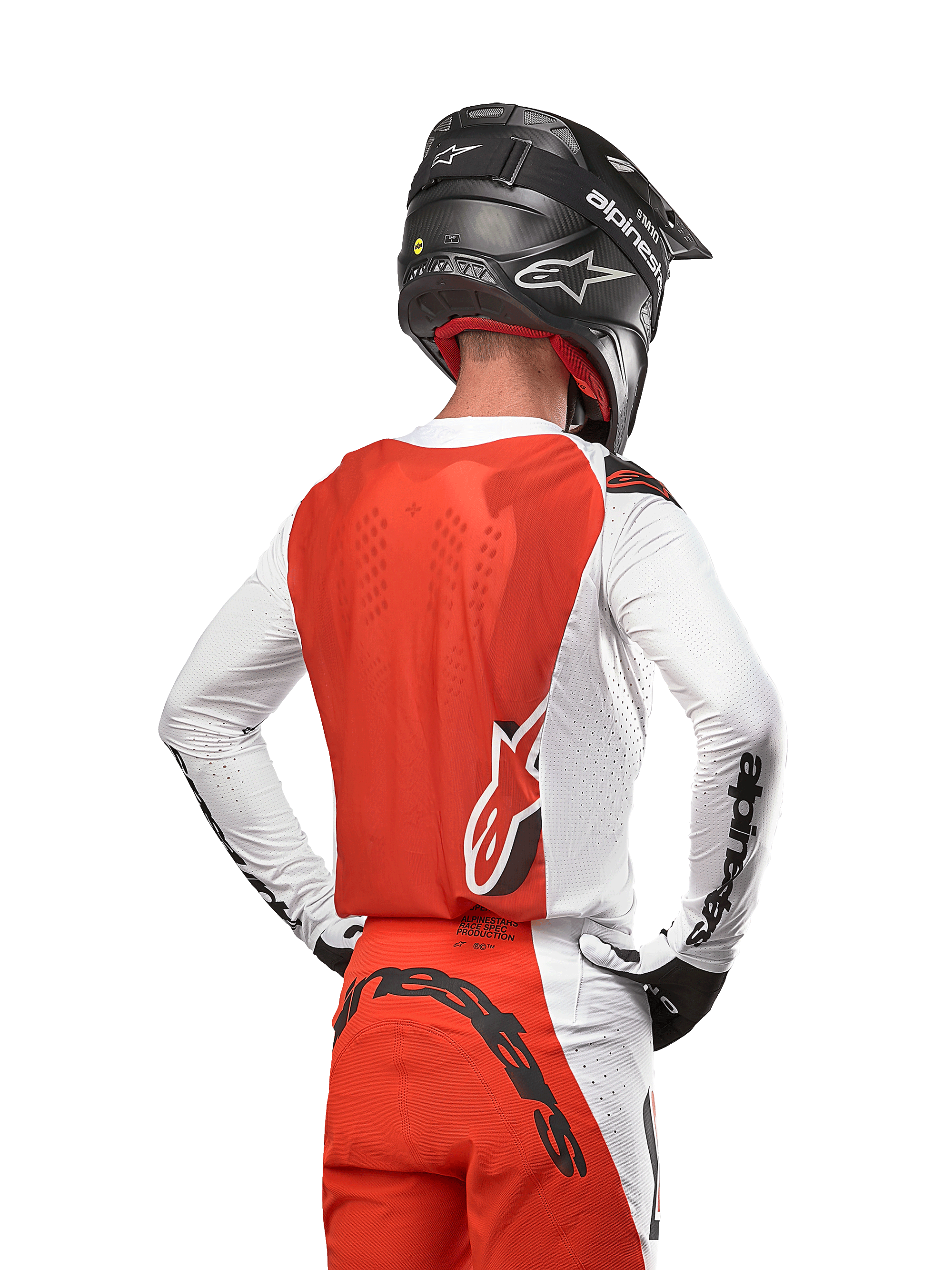 Piloto de motocross con el Jersey Alpinestars Supertech Ward 2024 en White Hot Orange, vista trasera que muestra el panel posterior naranja y mangas blancas con la marca en negro, combinado con pantalones a juego y casco negro, equipamiento profesional para carreras todoterreno