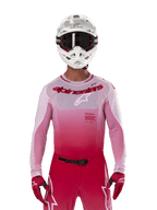 Piloto de motocross con el jersey Alpinestars 2024 Supertech Dade en Red Berry Lilac, pantalones a juego, casco blanco con gafas negras y guantes rojos, equipo de carreras profesional con tonos degradados en rosa y rojo