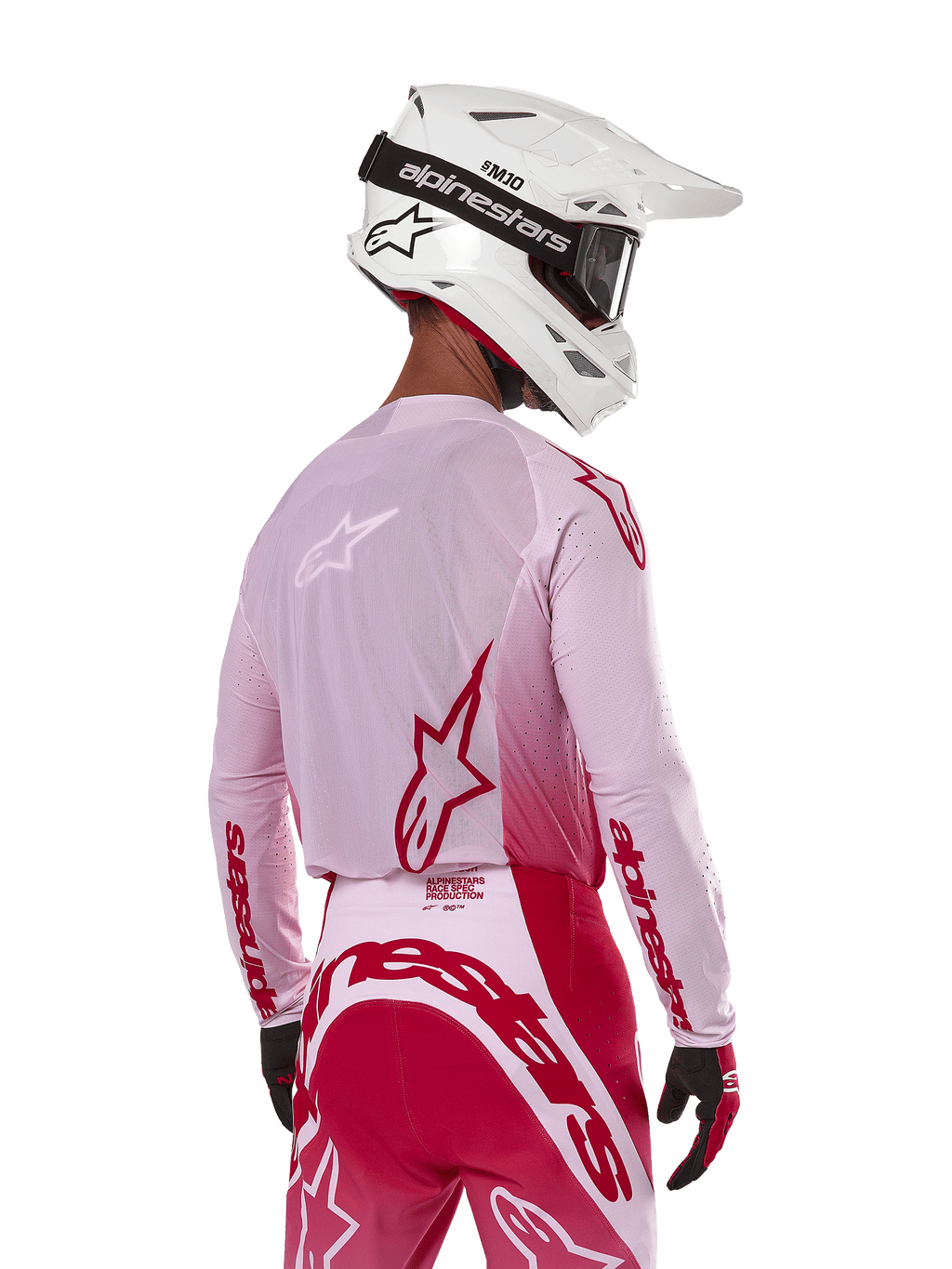 Piloto de motocross visto desde atrás con el Jersey Alpinestars 2024 Supertech Dade en Red Berry Lilac, con paneles de malla transpirable y logotipos Alpinestars en rojo, combinado con pantalones rojos y lila a juego y casco Alpinestars blanco con gafas, equipo profesional de carreras off-road