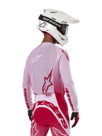 Piloto de motocross visto desde atrás con el Jersey Alpinestars 2024 Supertech Dade en Red Berry Lilac, con paneles de malla transpirable y logotipos Alpinestars en rojo, combinado con pantalones rojos y lila a juego y casco Alpinestars blanco con gafas, equipo profesional de carreras off-road