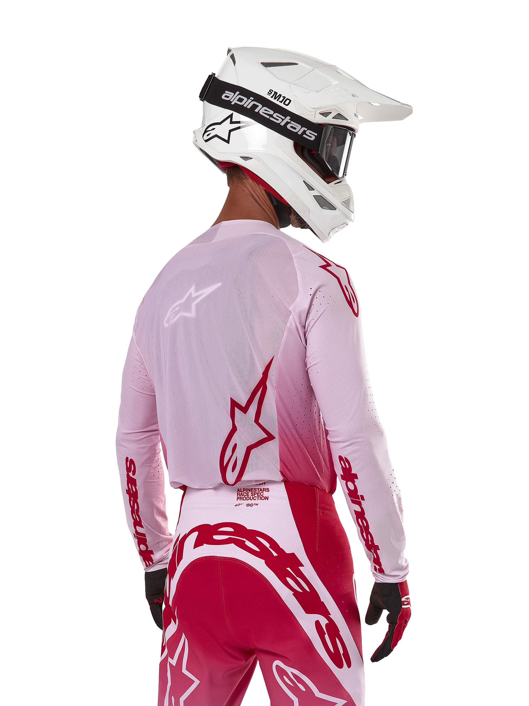 Piloto de motocross visto desde atrás con el Jersey Alpinestars 2024 Supertech Dade en Red Berry Lilac, con paneles de malla transpirable y logotipos Alpinestars en rojo, combinado con pantalones rojos y lila a juego y casco Alpinestars blanco con gafas, equipo profesional de carreras off-road