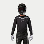 Alpinestars 2024 Fluid Graphite Jersey, Black and Silver motocross jersey, worn by a rider with a black helmet and red goggles, featuring silver Alpinestars branding on the chest, coordinated with black pants and white gloves for off-road performance.