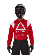 Motocross rider wearing Alpinestars Techdura Jersey, Bright Red with white graphics, featuring a large white triangle and ASTARS logo on the chest, paired with a black helmet, black goggles, and black riding gear, coordinated outfit for enduro and off-road racing